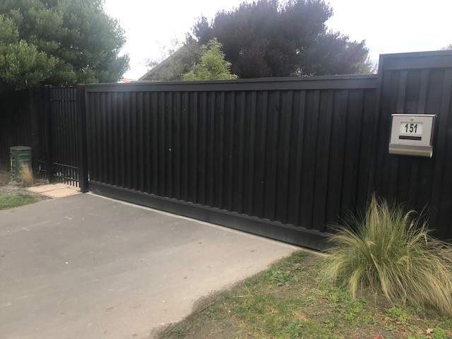 Black sliding driveway gate in solid vertical infill, matching the fence